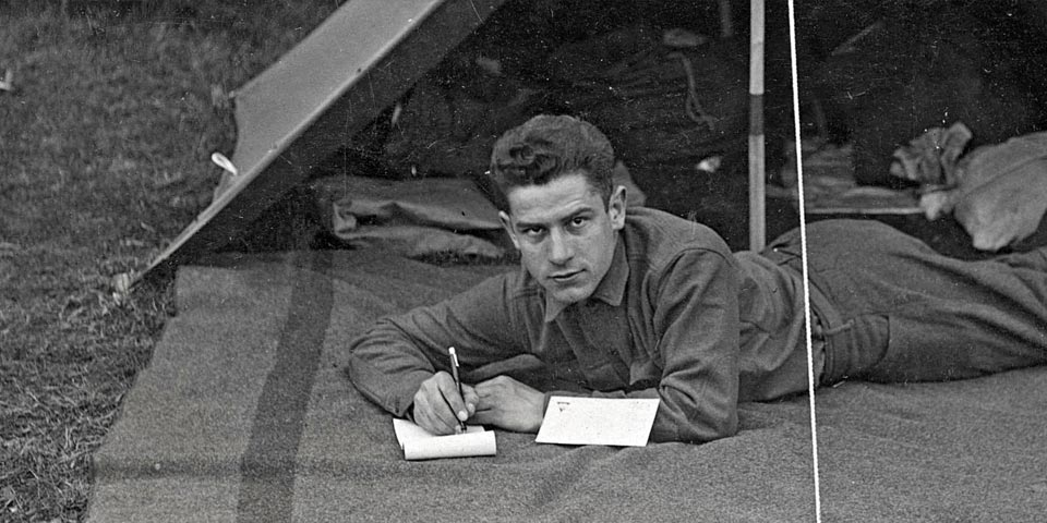 Man in uniform writing a letter on a blanket