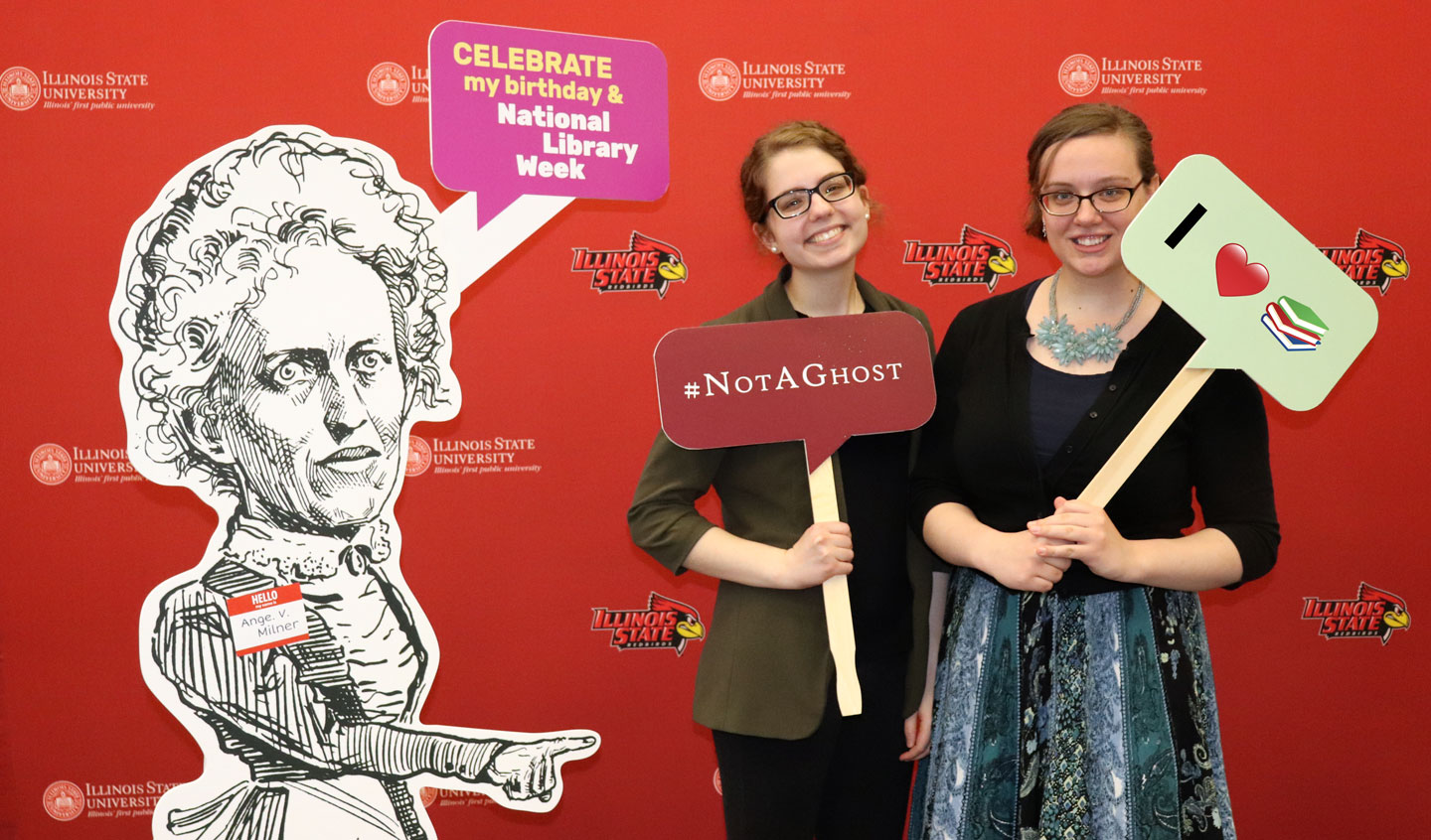 Two students posing with a cutout illustration of Ange Milner