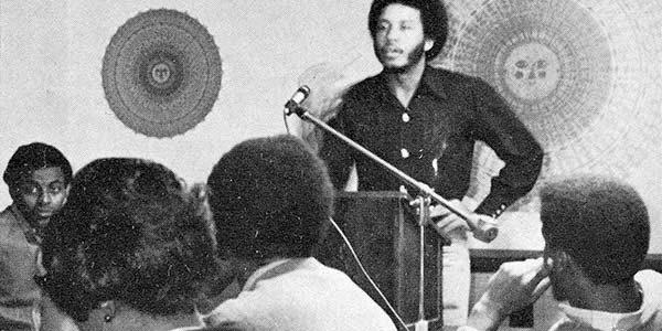 Black and white photo of a black man at a lectern.