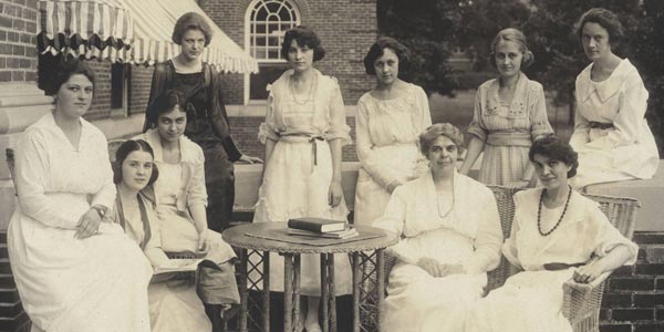 Black and white photograph of the 1920 Fell Hall honor residents at Illinois State Normal University. The photograph shows ten female honor students posing on a Fell Hall porch.  The cupola of Old Main is visible in the upper right corner of the photograph.