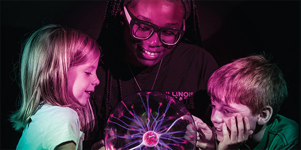 An adult showing two children a plasma globe