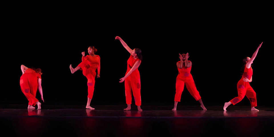 Five dancers in red clothing on a black background 