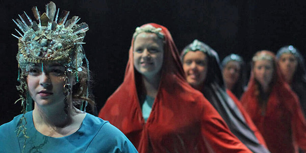 Performers in a line wearing red and blue costumes with intricate jewelery