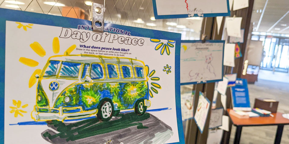 Illustration of a tie-dyed VW bus on a postcard in front of a wall covered in hand drawn postcards
