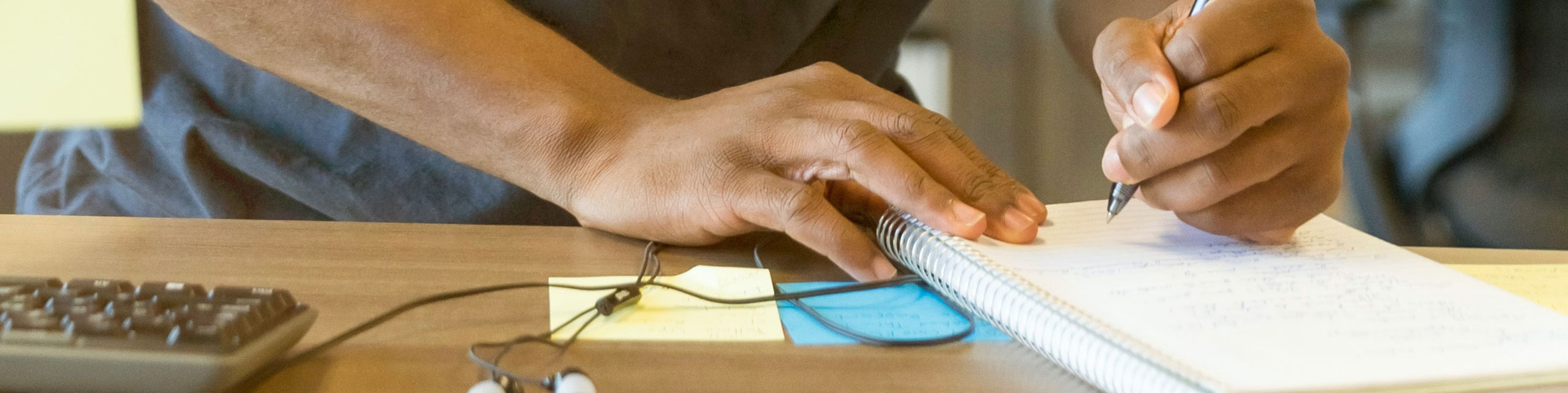 An individual writing on a jotter with a pen